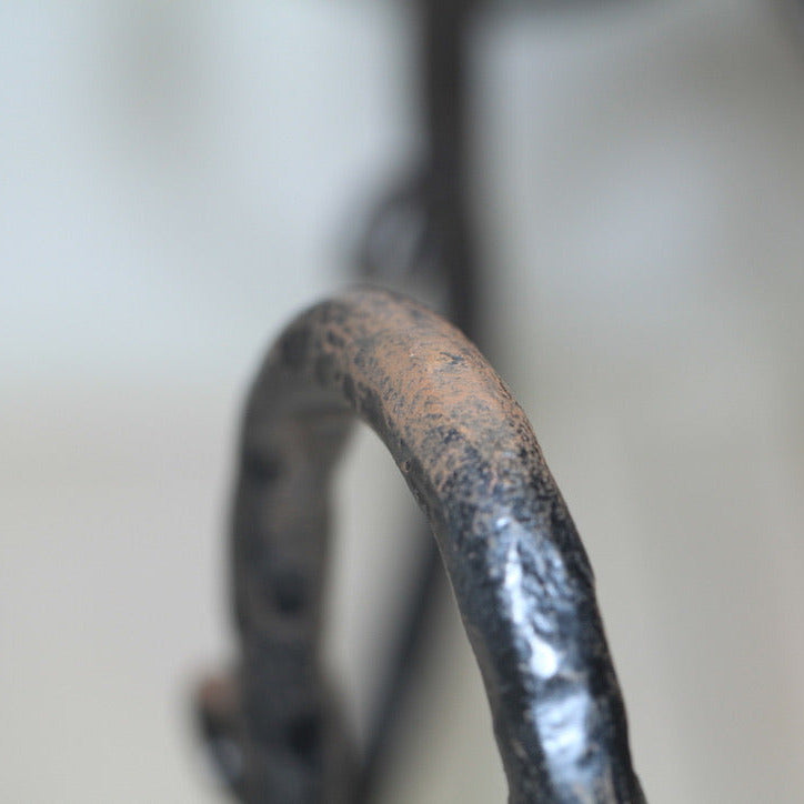 Close-up detail of hand-wrought iron candelabra arm showing textured forged surface and aged patina.