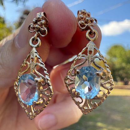 Vintage 14K gold filigree aquamarine drop earrings held outdoors against a blurred natural background