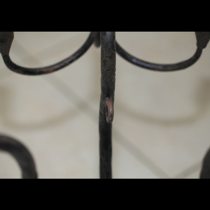Close-up detail of the wrought iron candelabra stem and curved arms with aged patina.