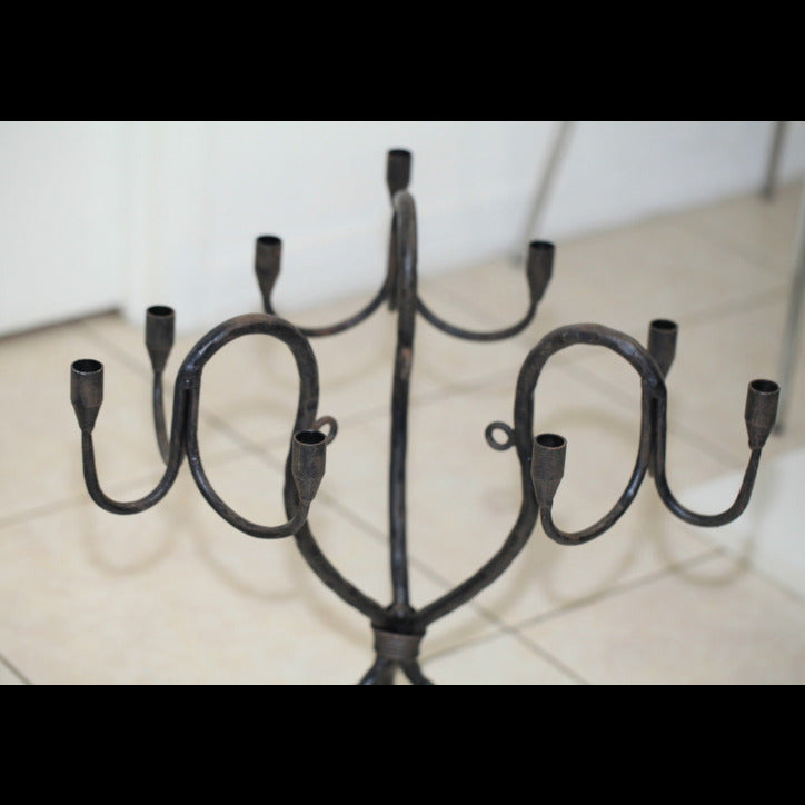 Wrought iron candelabra with multiple curved arms and candle cups, shown from above on a tiled floor.