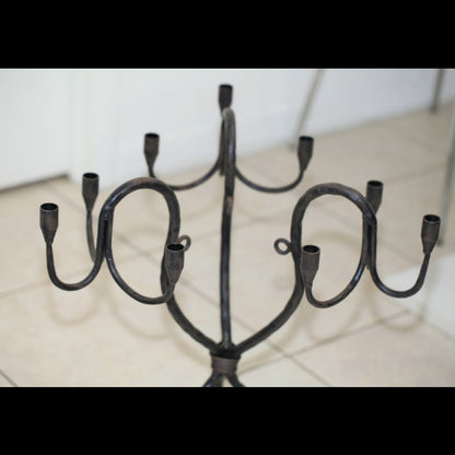 Wrought iron candelabra with multiple curved arms and candle cups, shown from above on a tiled floor.
