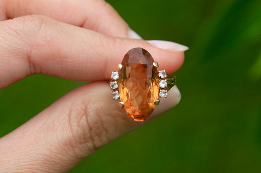 Vintage 1950s 14K gold oval citrine and diamond cocktail ring held in hand against green background