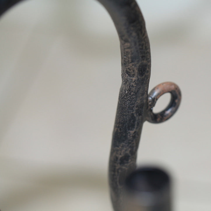 Close-up detail of hand-wrought iron candelabra arm showing textured forged surface and aged patina.