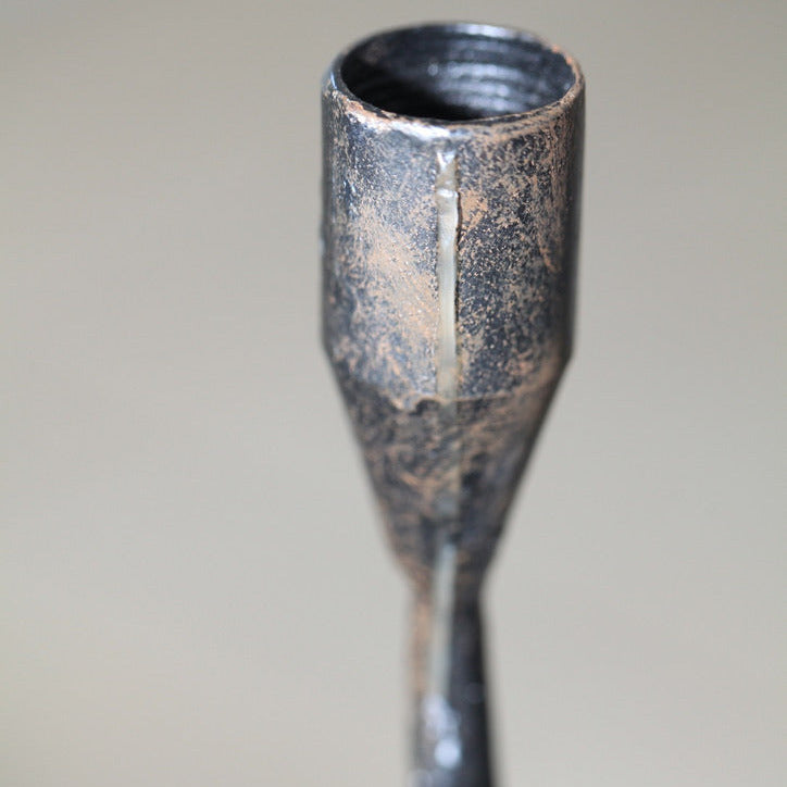 Close-up of hand-forged iron candle cup with visible seams, aged patina, and textured surface.