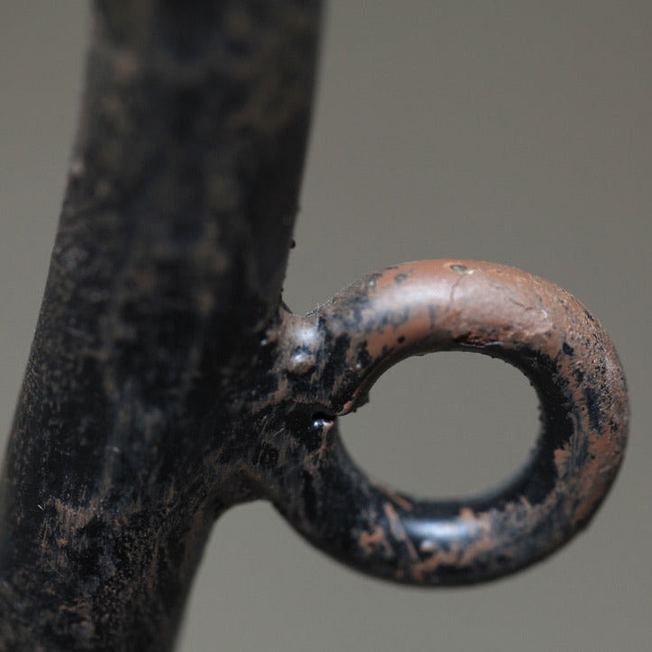 Close-up of a hand-forged iron candle cup showing aged patina and textured surface.