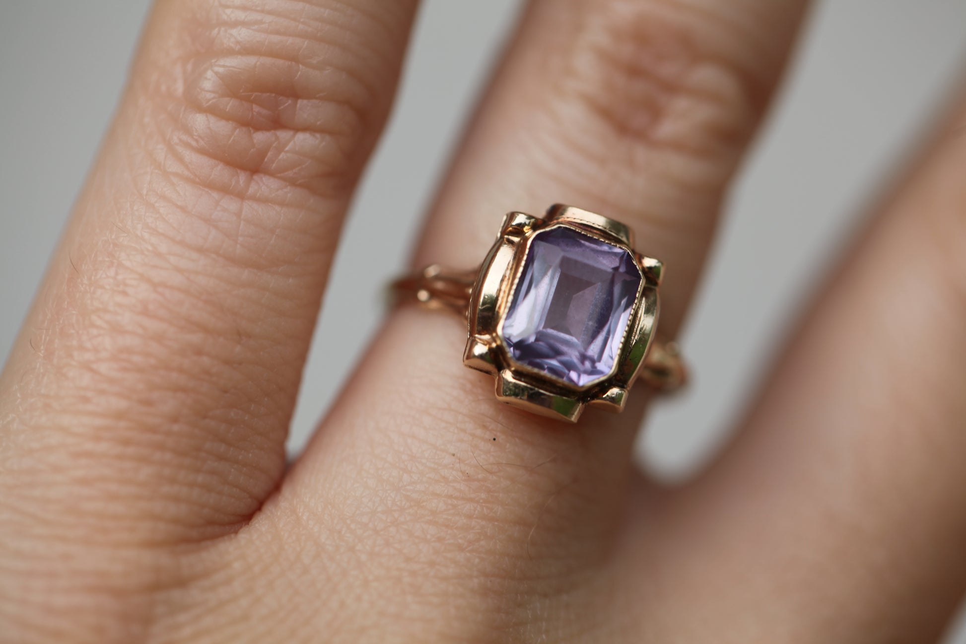 Close-up of a vintage mid-century 10K yellow gold ring with an emerald-cut lavender amethyst, worn on a finger against a neutral background.