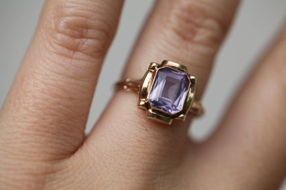 Close-up of a vintage mid-century 10K yellow gold ring with an emerald-cut lavender amethyst, worn on a finger against a neutral background.