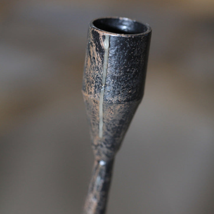 Close-up of hand-forged iron candle cup with visible seams, aged patina, and textured surface.