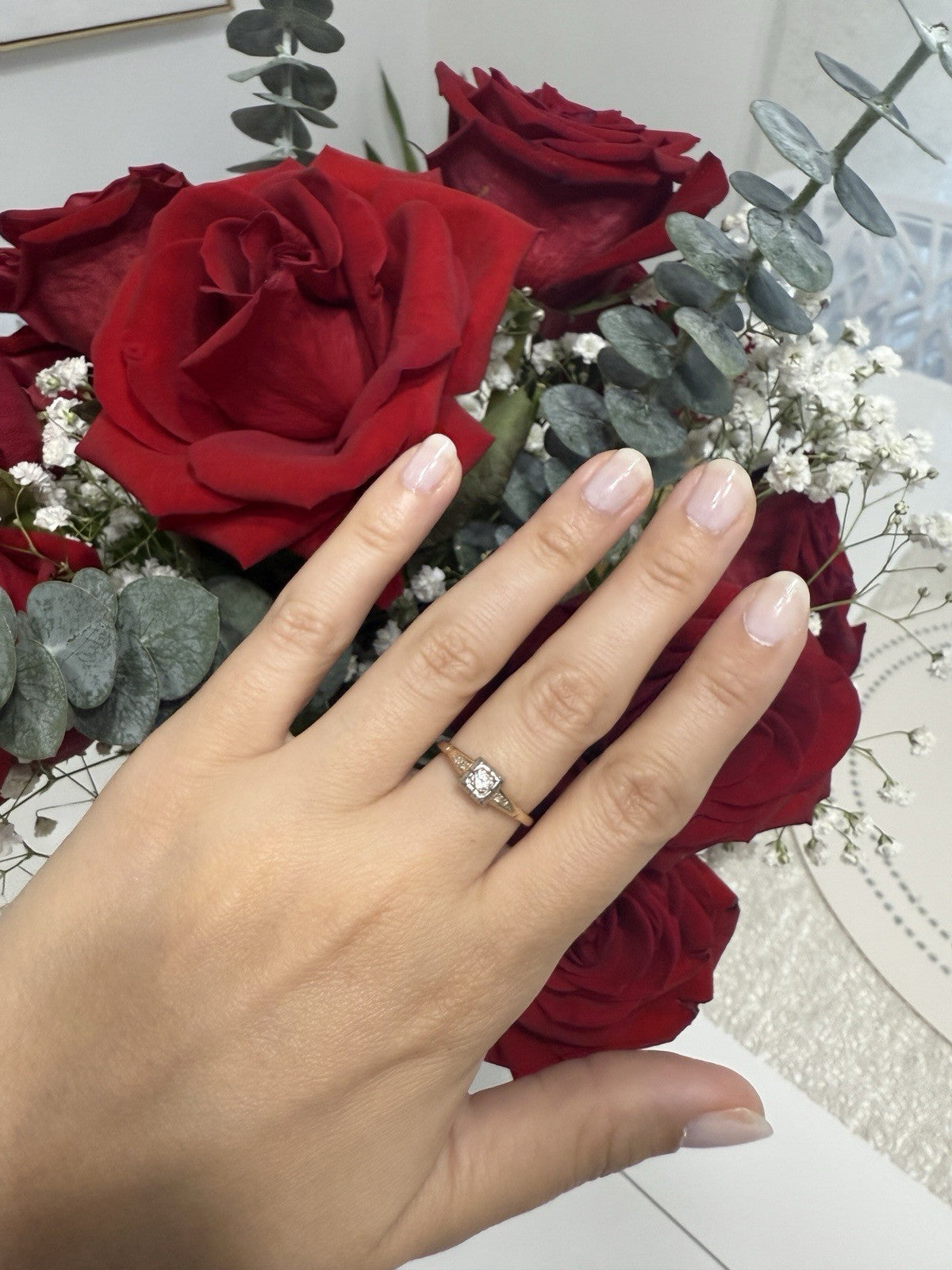 Hand wearing 1930s Art Deco ArtCarved 14K two-tone diamond ring with old European cut, styled with red roses and greenery