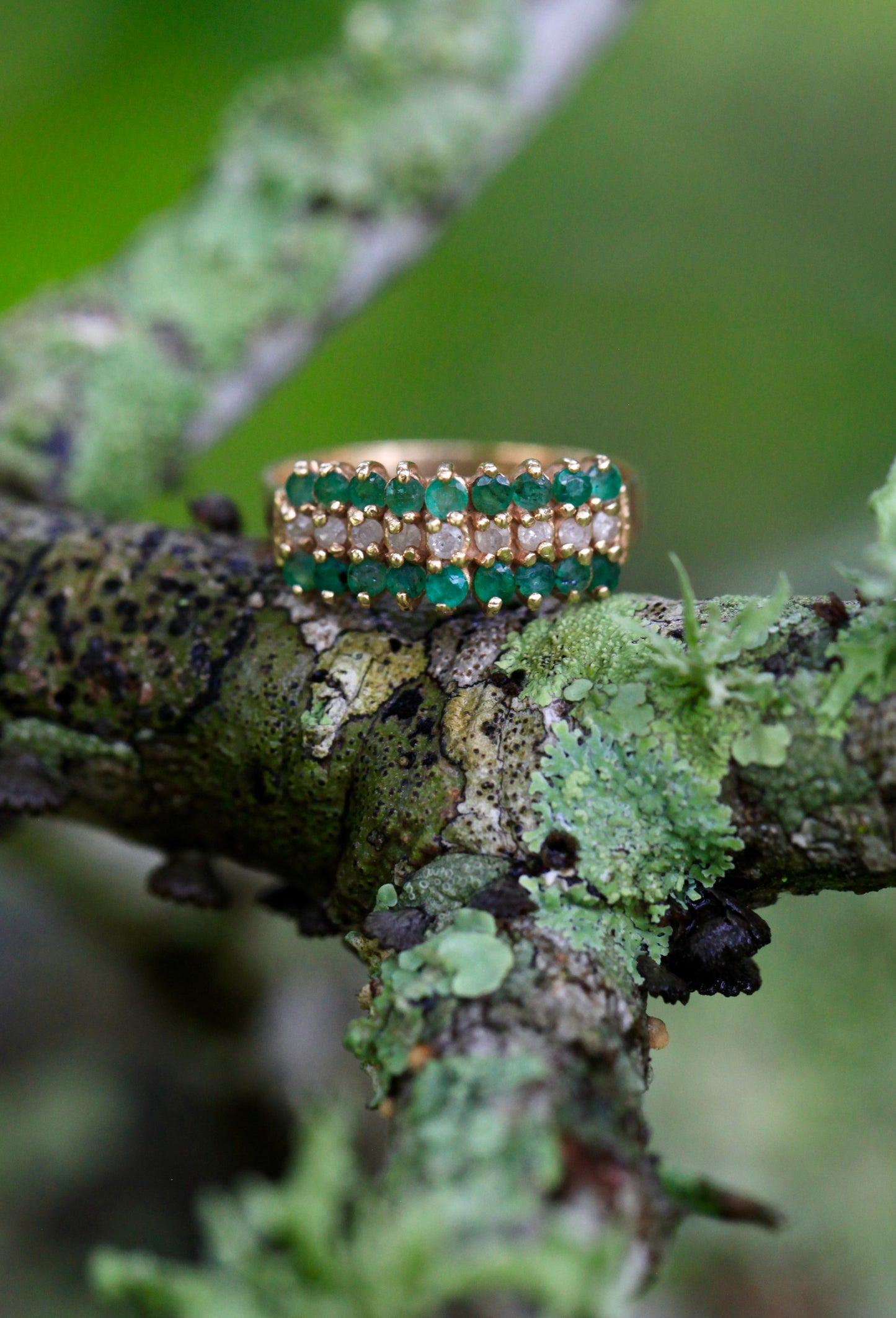 Vintage 14K yellow gold emerald and diamond cocktail cluster ring displayed on mossy branch with green foliage background