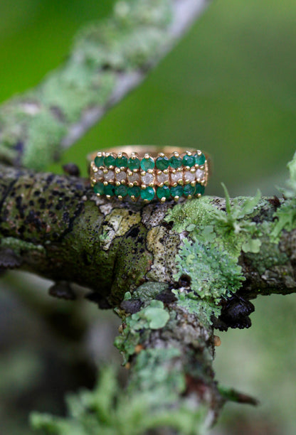 Vintage 14K yellow gold emerald and diamond cocktail cluster ring displayed on mossy branch with green foliage background