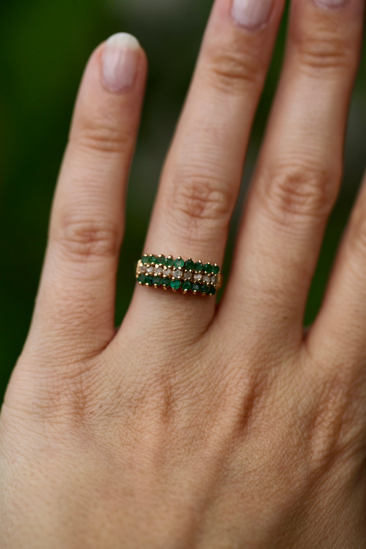 Vintage 14K yellow gold emerald and diamond pyramid cocktail ring worn on hand outdoors with blurred green background
