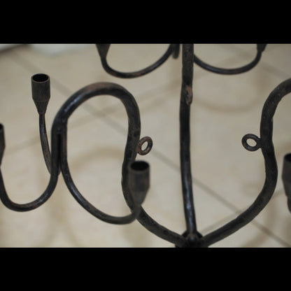 Close-up detail of a wrought iron candelabra showing curved arms and candle cups against a neutral background.