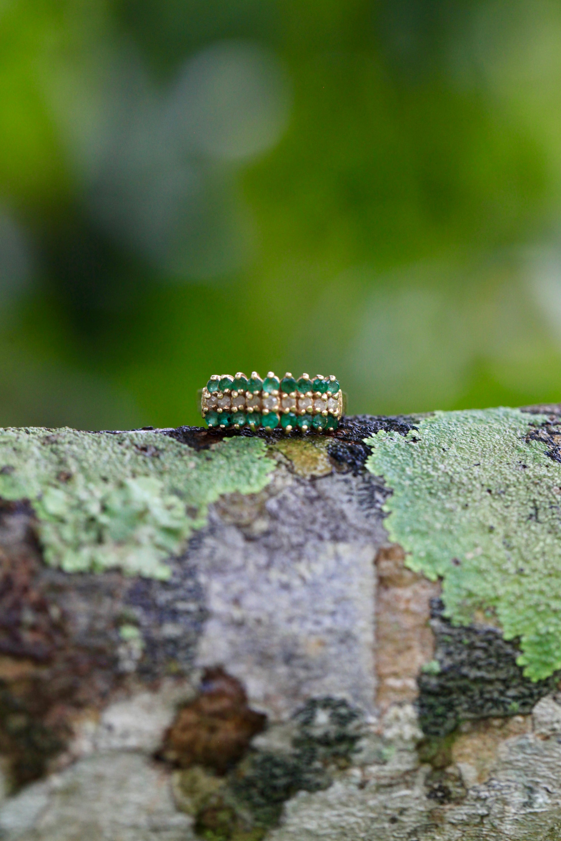 Vintage 14K yellow gold emerald and diamond pyramid cocktail ring displayed on textured tree bark with blurred green background