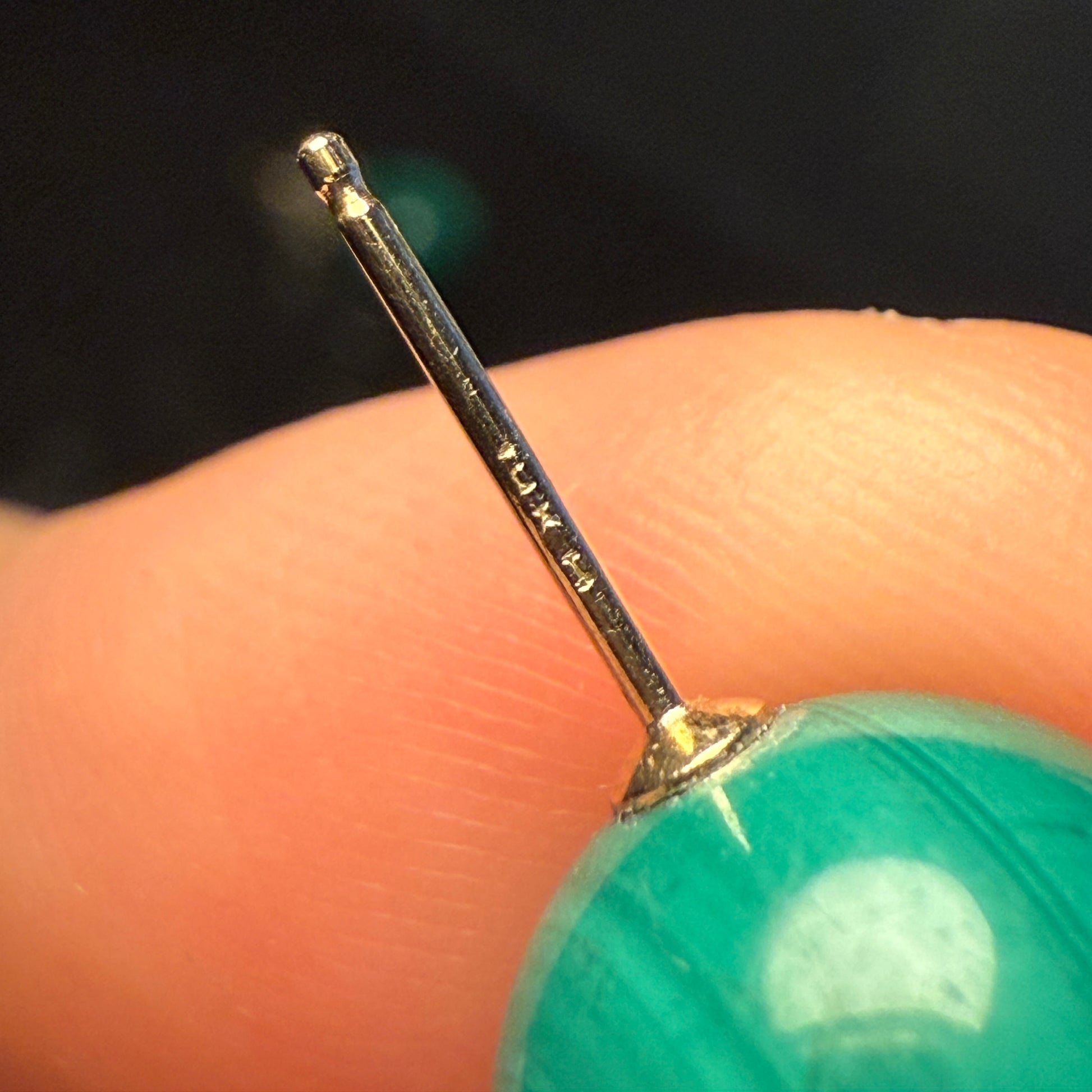 Macro close-up of a 14K gold earring post showing the 14K stamp on a malachite stud