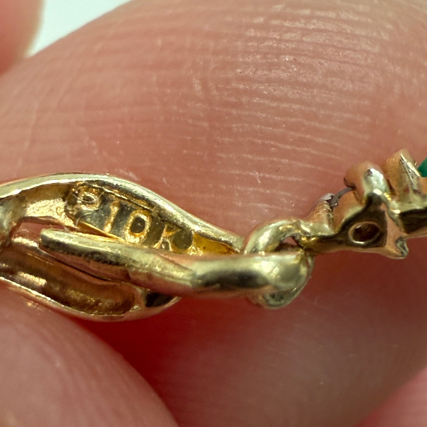 Close-up of 10K gold hallmark on vintage emerald dangle earring held between fingers