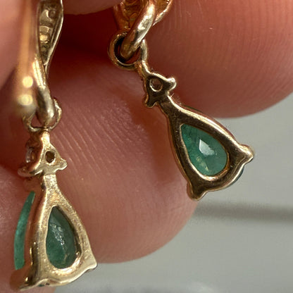 Close-up of vintage 10K yellow gold emerald dangle earrings showing open-back teardrop settings