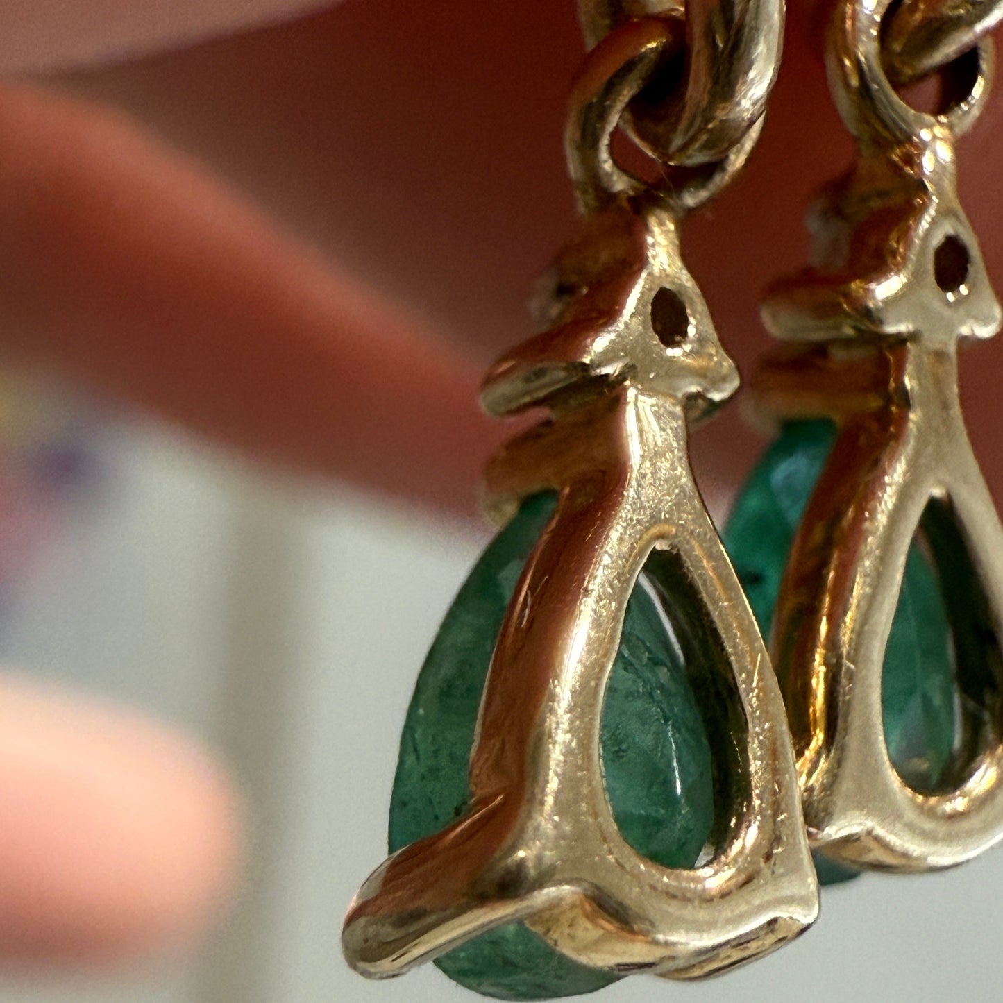 Close-up of vintage 10K yellow gold emerald dangle earrings showing open-back teardrop settings