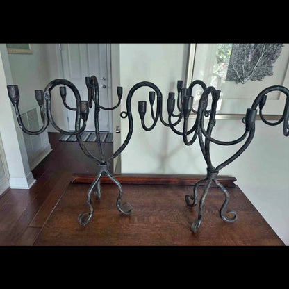 Pair of vintage hand-wrought iron candelabra with scrolling forged arms, photographed indoors on a dark wooden floor.