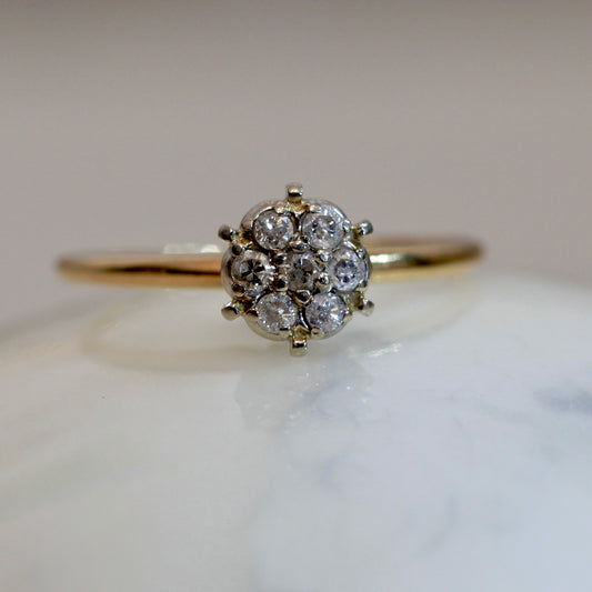 1950s vintage 10K two-tone gold floral cluster engagement ring with seven round diamonds, displayed on white marble surface