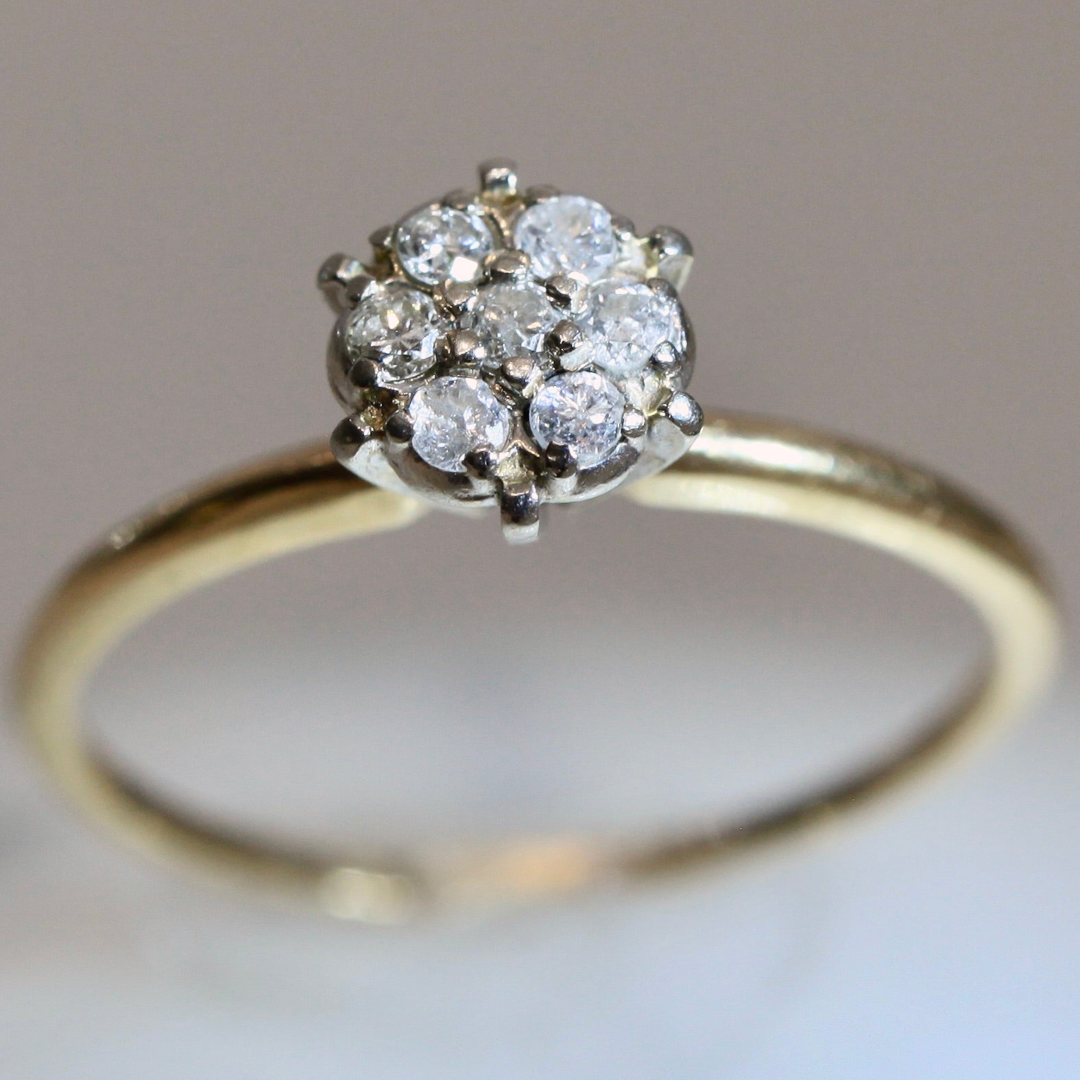 Close-up of 1950s vintage 10K two-tone gold floral cluster engagement ring with seven round diamonds, illusion head design on neutral background