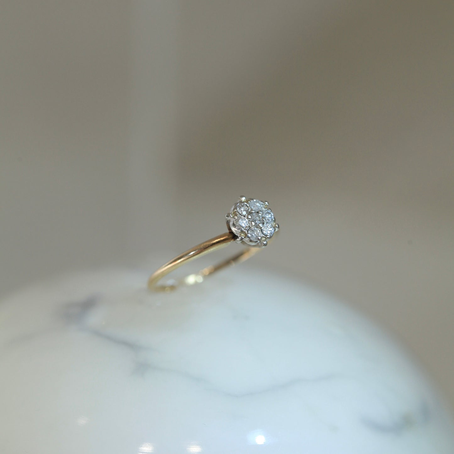 1950s vintage 10K two-tone gold engagement ring with seven-diamond floral cluster, displayed upright on white marble surface with soft neutral background