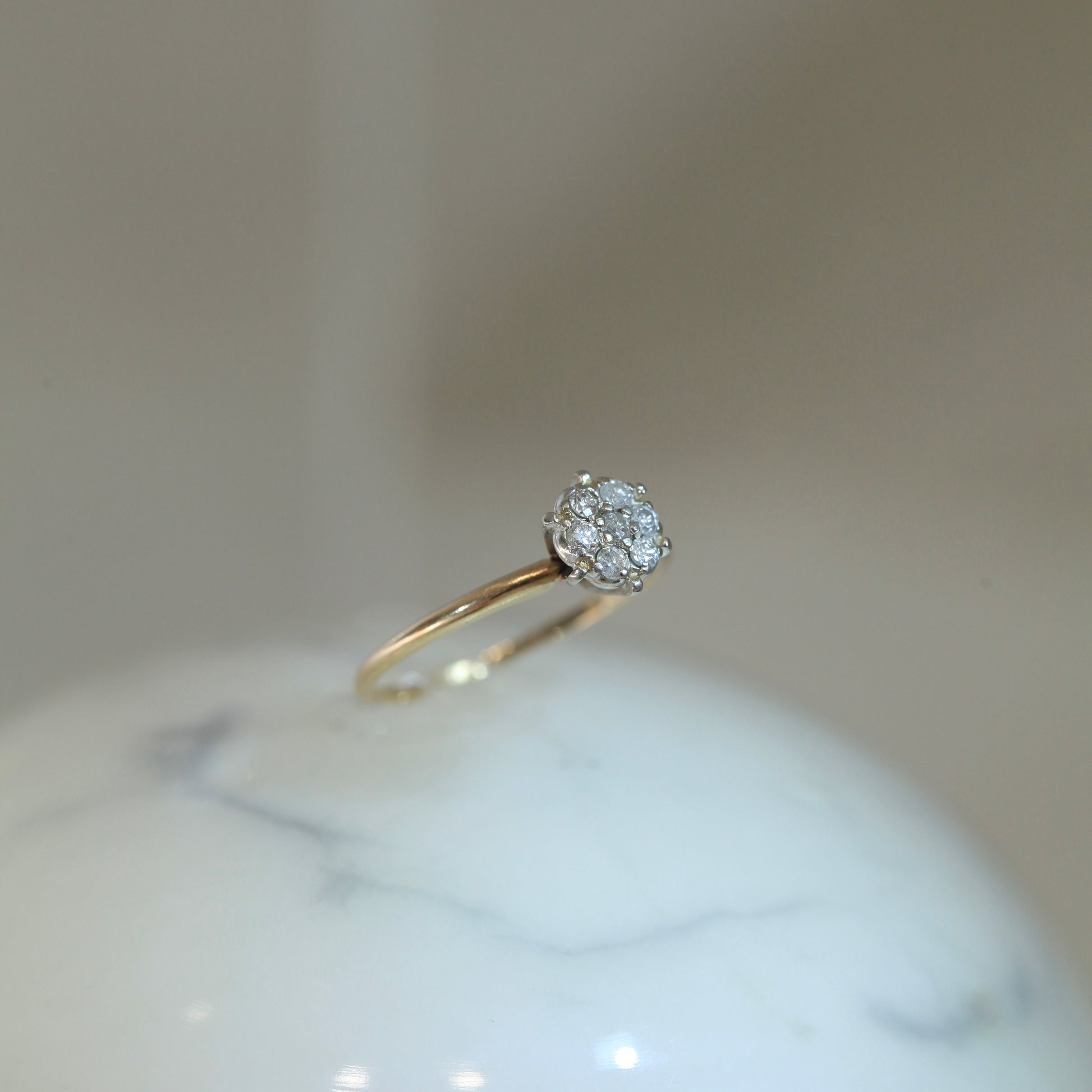 1950s vintage 10K two-tone gold engagement ring with seven-diamond floral cluster, displayed upright on white marble surface with soft neutral background