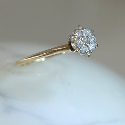 Angled view of 1950s vintage 10K two-tone gold engagement ring with seven-diamond floral cluster, slim yellow gold band on white marble surface