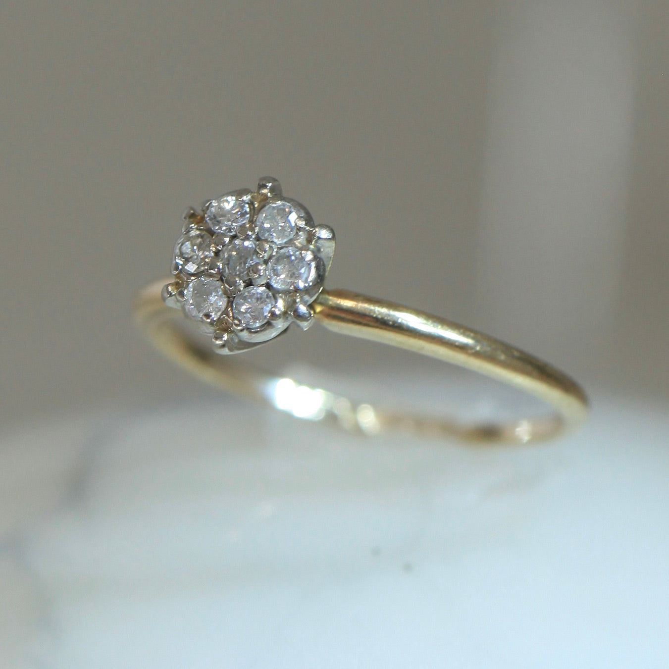 Close-up of 1950s vintage 10K two-tone gold engagement ring with seven-diamond floral cluster on marble surface, slim band highlighted in soft light