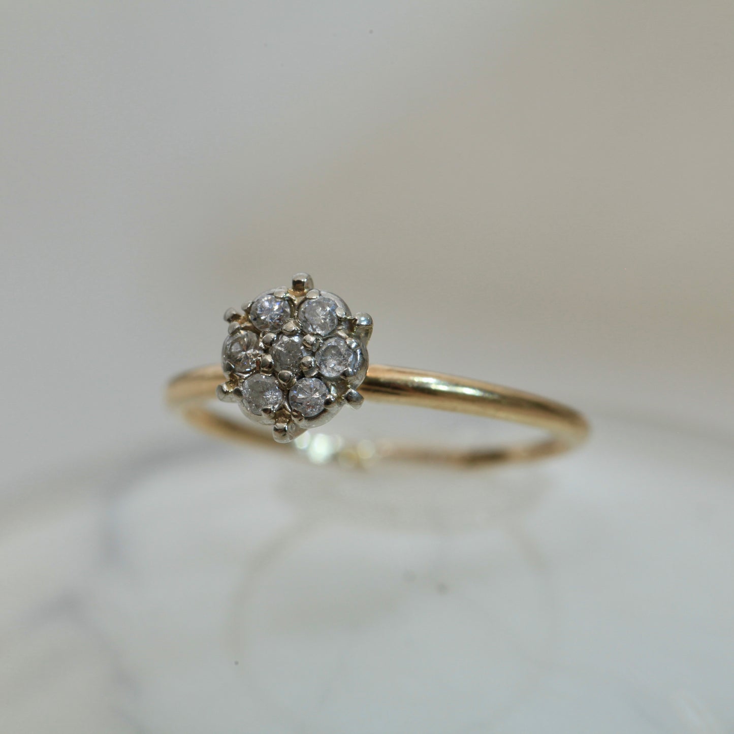 1950s vintage 10K two-tone gold engagement ring with seven-diamond floral cluster, photographed on a light marble surface with soft background