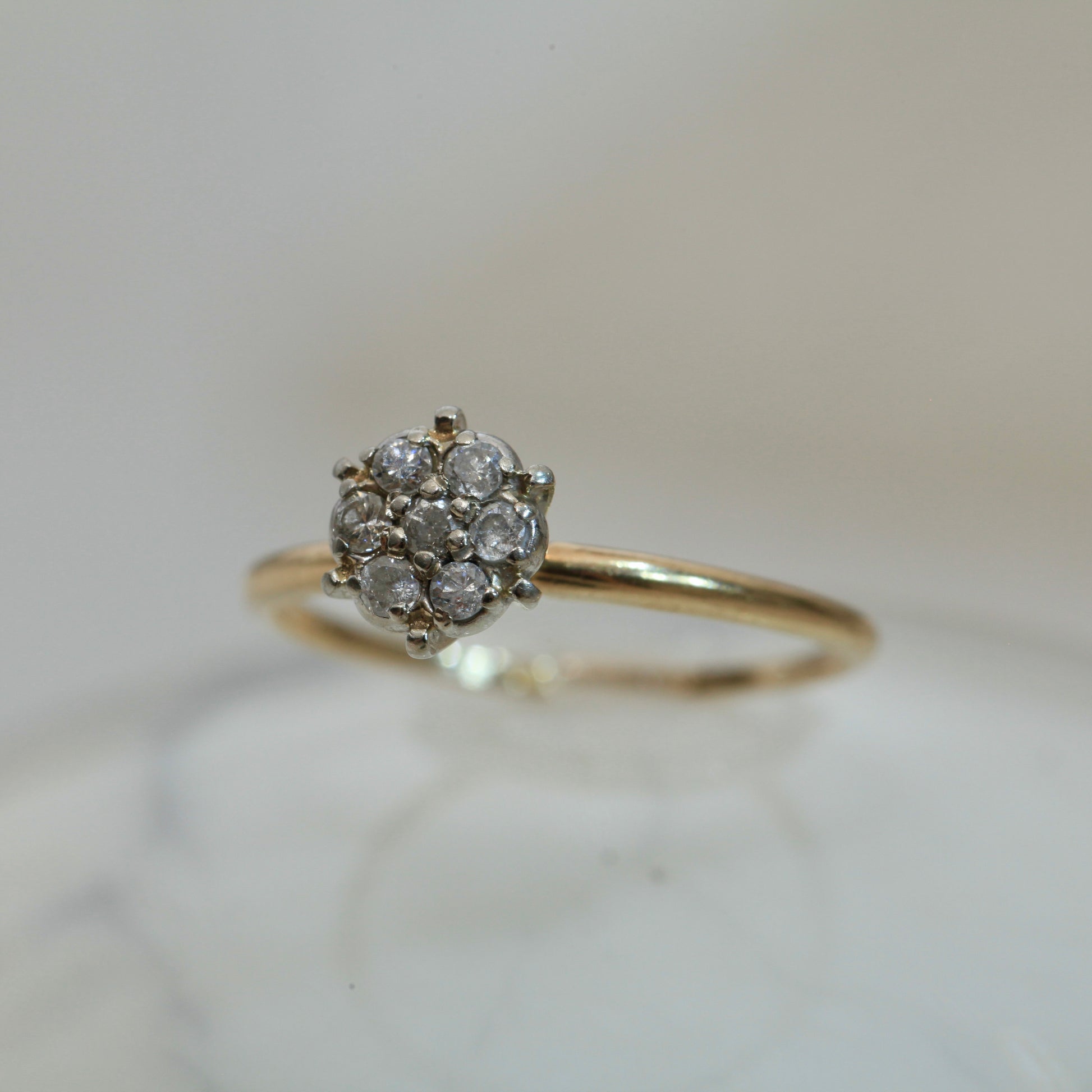 1950s vintage 10K two-tone gold engagement ring with seven-diamond floral cluster, photographed on a light marble surface with soft background