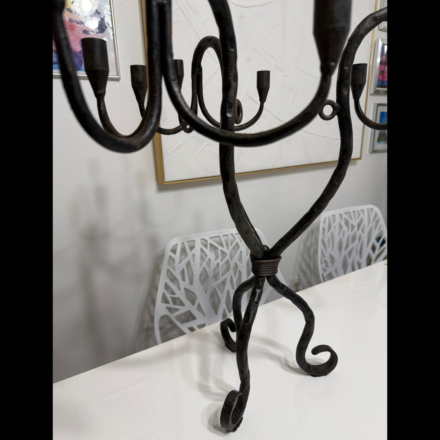 Wrought iron candelabra standing on a white tabletop, showing curved arms, candle cups, and sculptural tripod base.
