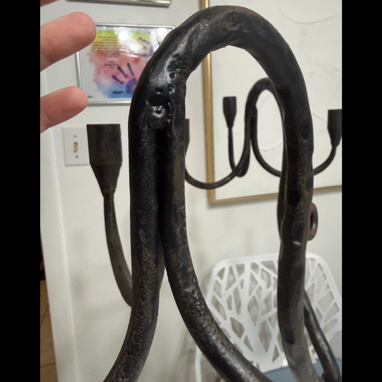 Close-up of a curved wrought iron candelabra arm with dark patina in an indoor setting.
