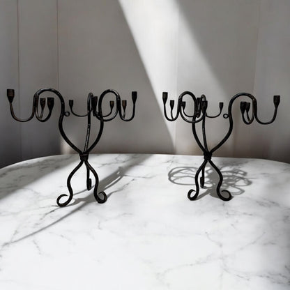 Pair of vintage hand-wrought iron candelabra with scrolling forged arms, displayed on a white marble surface in soft natural light.