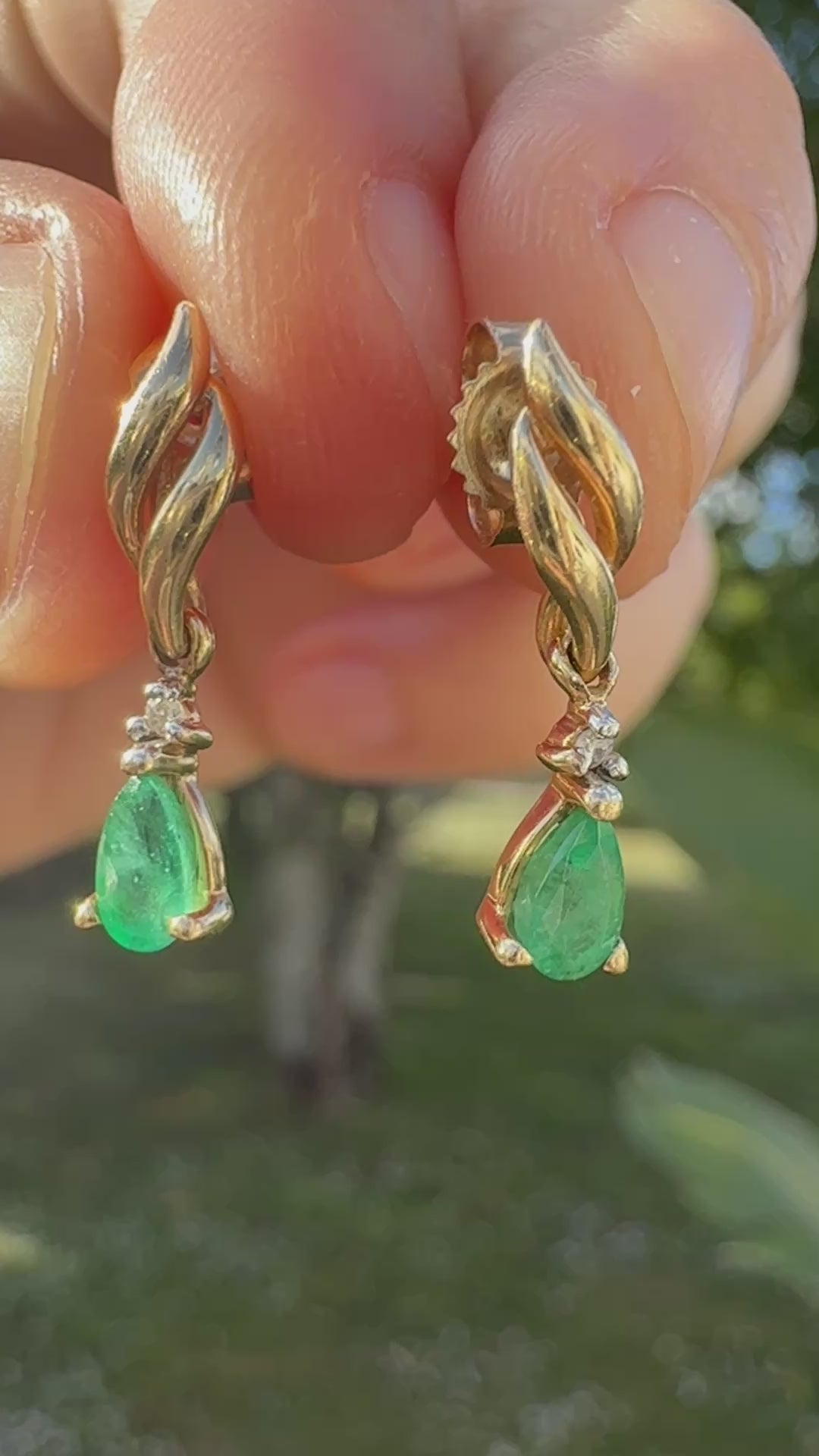Hand holding pair of 1990s vintage 10K yellow gold emerald and diamond dangle earrings outdoors