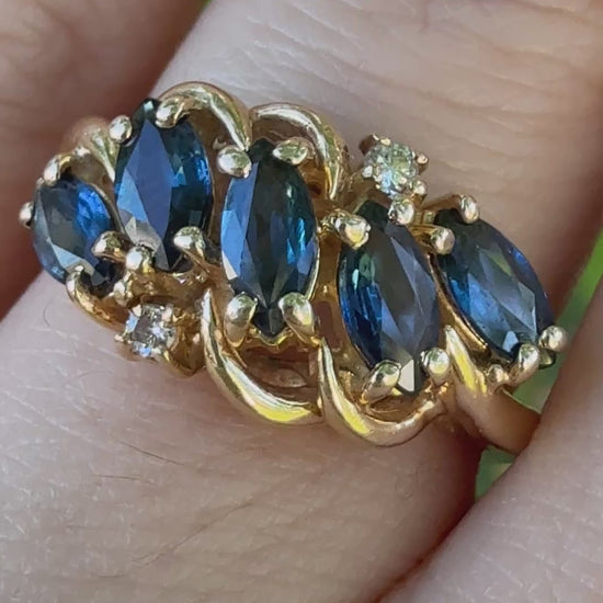 Video showing vintage 1960s 14K gold swirl bypass ring with five marquise blue sapphires and diamonds worn on a hand, capturing sparkle in natural light.”