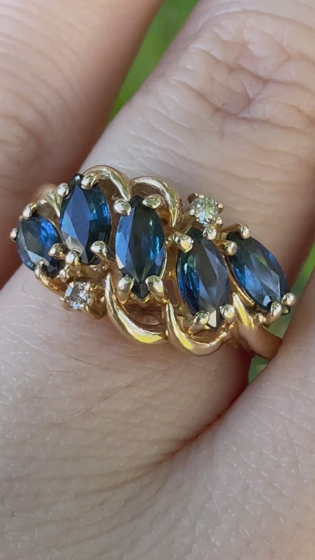 Video showing vintage 1960s 14K gold swirl bypass ring with five marquise blue sapphires and diamonds worn on a hand, capturing sparkle in natural light.”