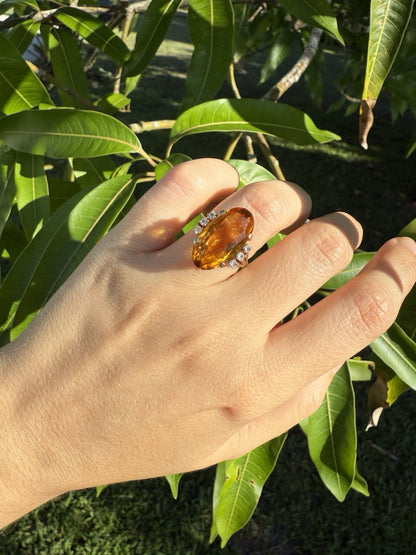 Hand wearing vintage 1950s 14K gold citrine and diamond cocktail ring outdoors against green leaves