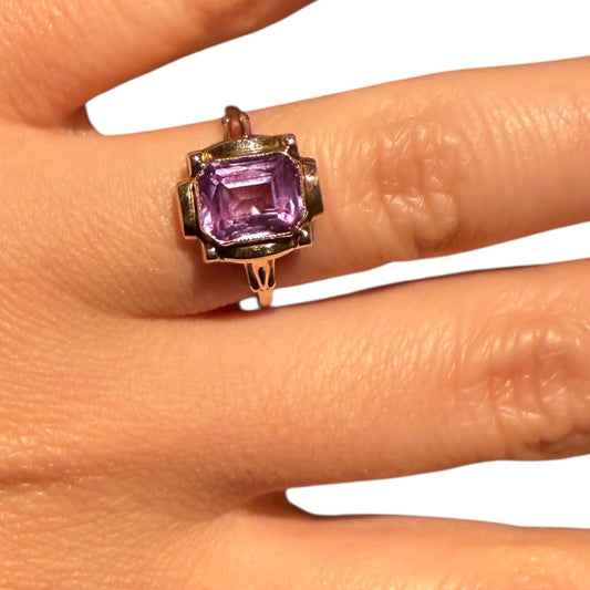 Vintage 1950s 10K yellow gold ring with an emerald-cut lavender amethyst, worn on a finger against a white background.
