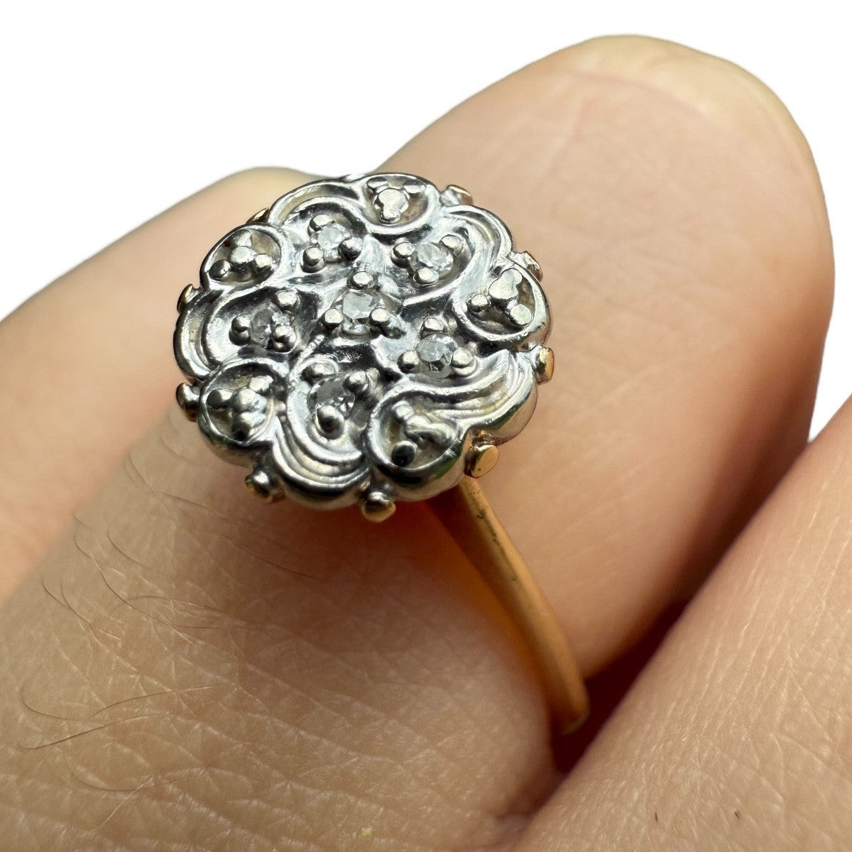 Close-up of 1950s vintage 10K gold diamond illusion cluster ring with ornate flower motif, shown on finger against white background.