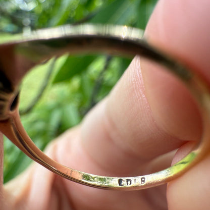Close-up of vintage 1950s 10K gold diamond illusion cluster ring band showing clear maker’s mark “CD 18,” held between fingers with blurred green background.
