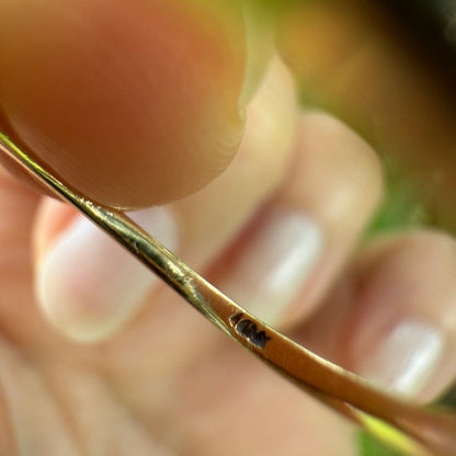 Close-up of vintage 1950s 10K gold diamond illusion cluster ring band showing faint hallmark stamp, held between fingers with blurred green background.