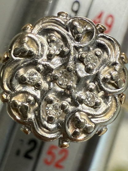 Close-up of 1950s vintage 10K gold diamond illusion cluster ring with six diamonds in ornate white gold swirl design, shown on a ring mandrel with size markings in background.
