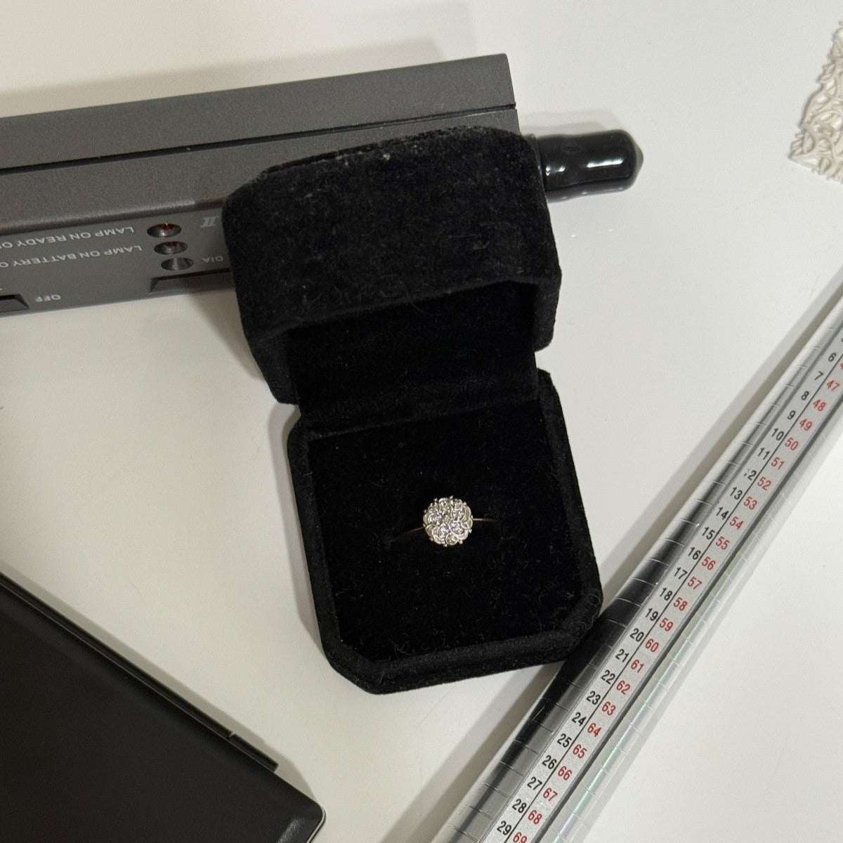 Vintage 1950s 10K gold diamond illusion cluster ring in black velvet box, shown on white surface with ring mandrel for scale.