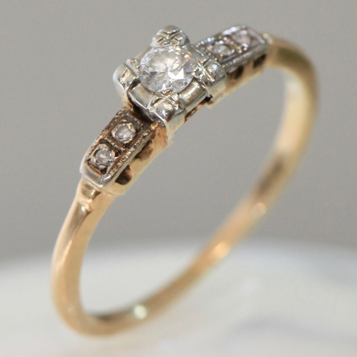 1940s vintage 14K two-tone diamond engagement ring with illusion-set center and stepped shoulders, photographed on white background.