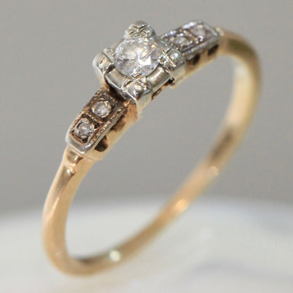 1940s vintage 14K two-tone diamond engagement ring with illusion-set center and stepped shoulders, photographed on white background.