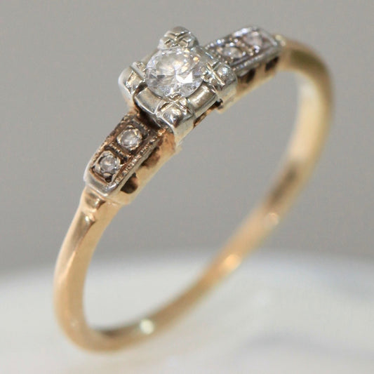 1940s vintage 14K two-tone diamond engagement ring with illusion-set center and stepped shoulders, photographed on white background.