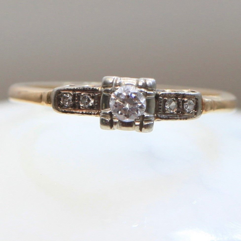 Front view of 1940s vintage 14K two-tone diamond engagement ring with illusion-set center and stepped shoulders, photographed on white background.