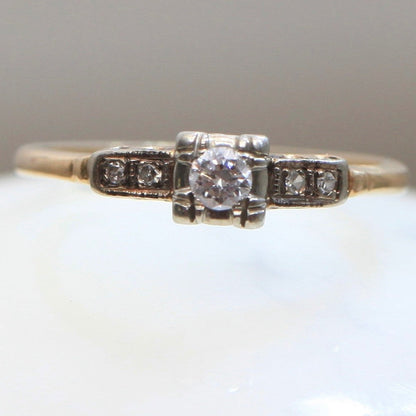 Front view of 1940s vintage 14K two-tone diamond engagement ring with illusion-set center and stepped shoulders, photographed on white background.