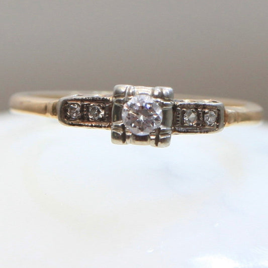 Front view of 1940s vintage 14K two-tone diamond engagement ring with illusion-set center and stepped shoulders, photographed on white background.